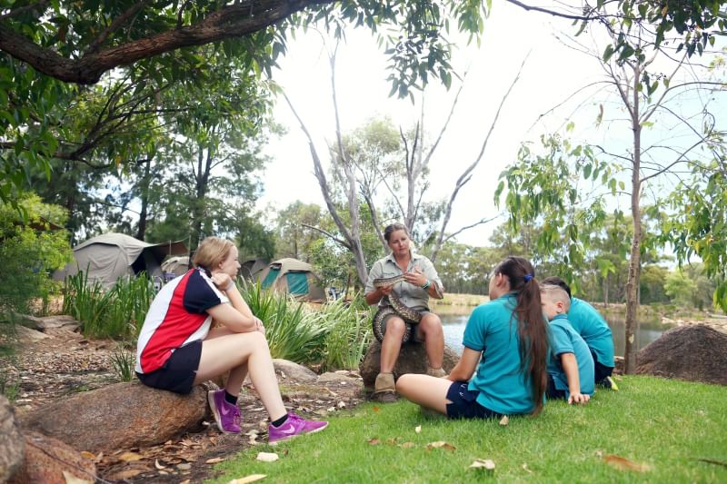 A small group of students with Taronga educator sitting on rocks in outside learning space at Taronga Western Plains Zoo
