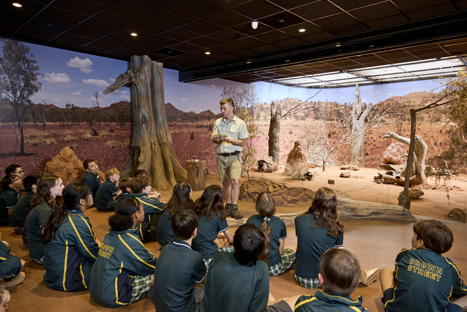 Students seated indoors listening to a guide in a desert-themed immersive classroom.