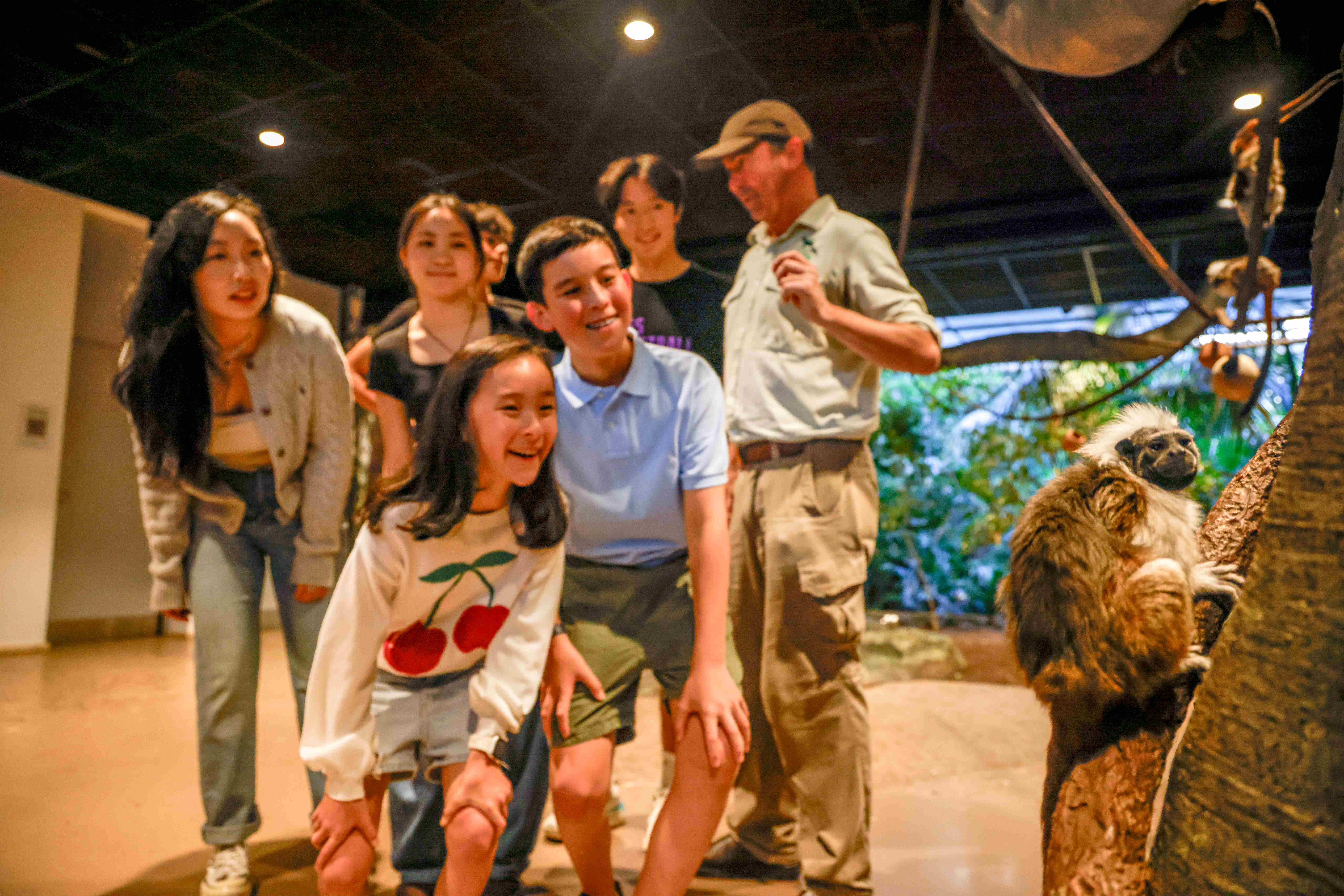 School students observing a monkey climbing in an immersive classroom while an educator stands nearby.
