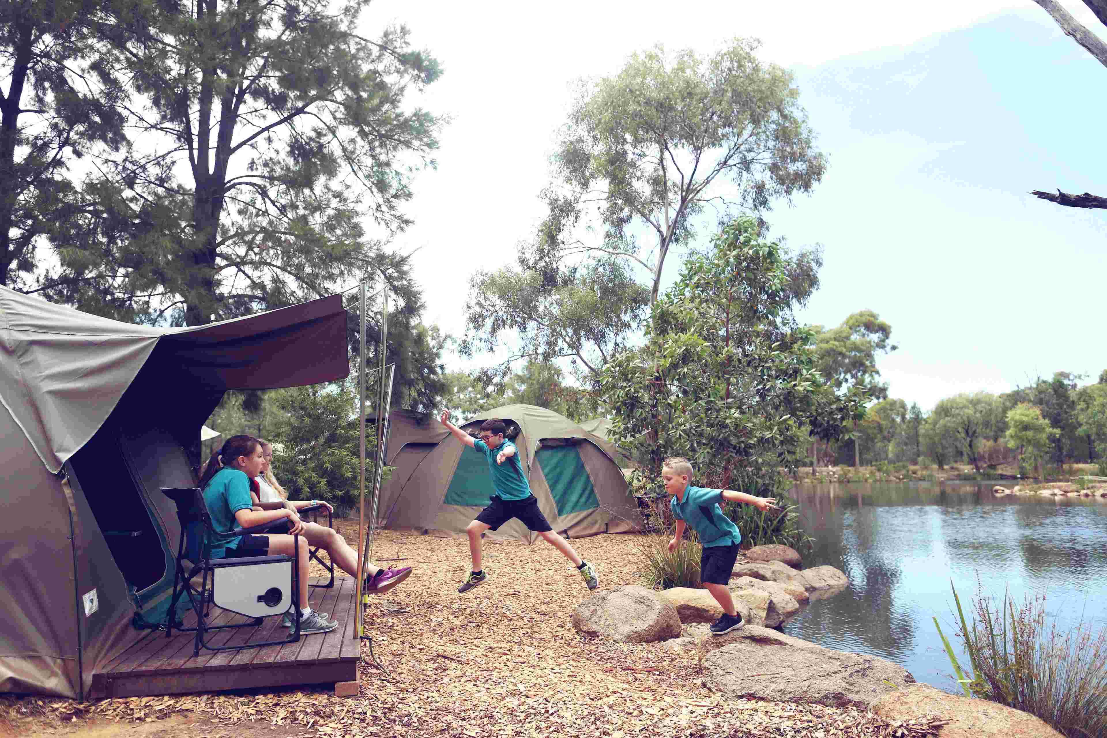 Students enjoying outdoor activities near safari‑style tents during a Zoosnooz overnight education program. near billabong